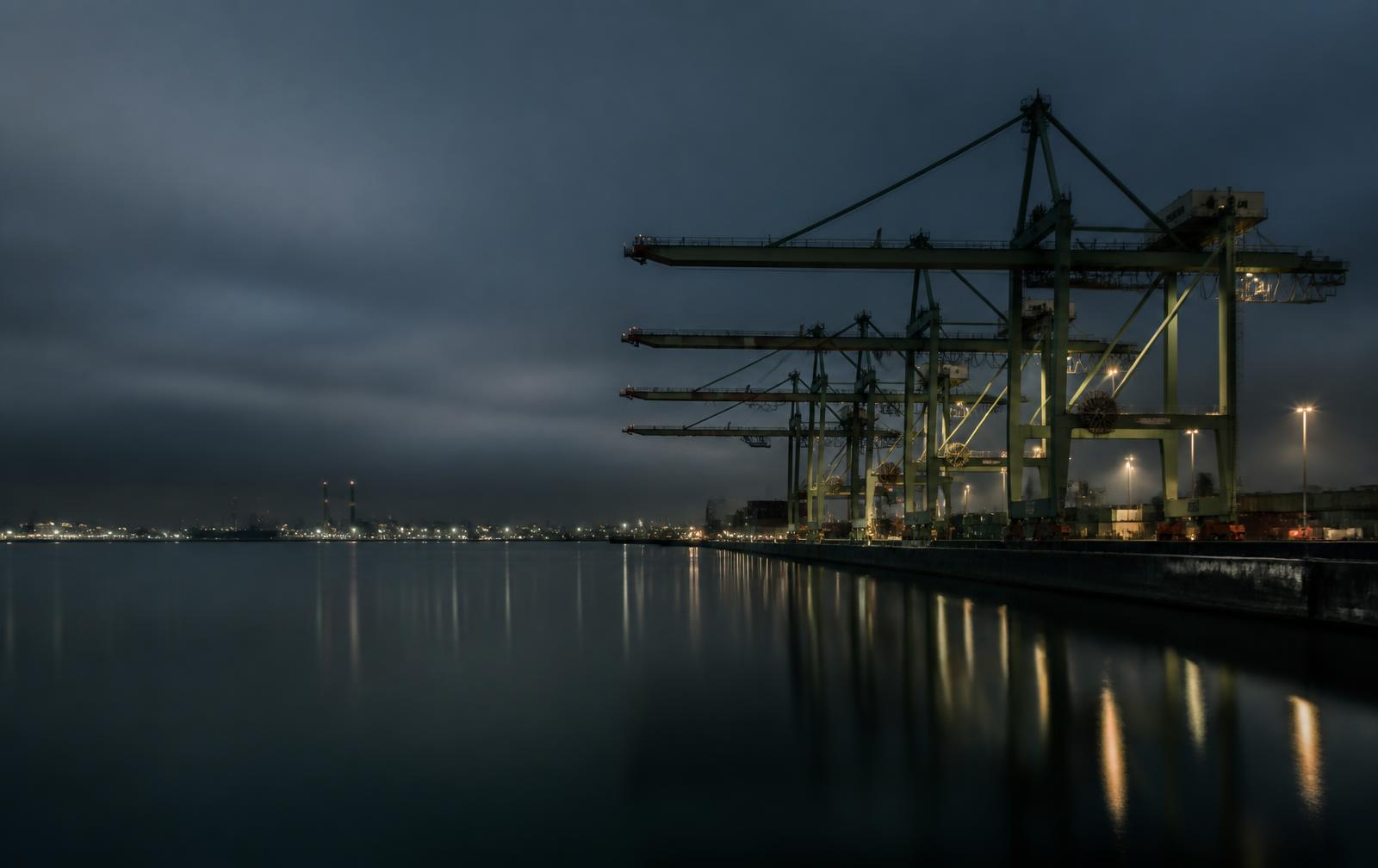 Port cranes reflected in still water at blue hour